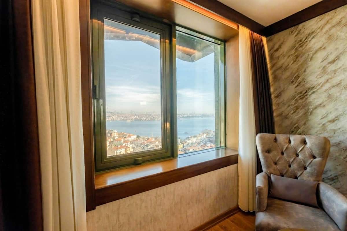 A room with a large window, a cushioned armchair, and a marble wall.