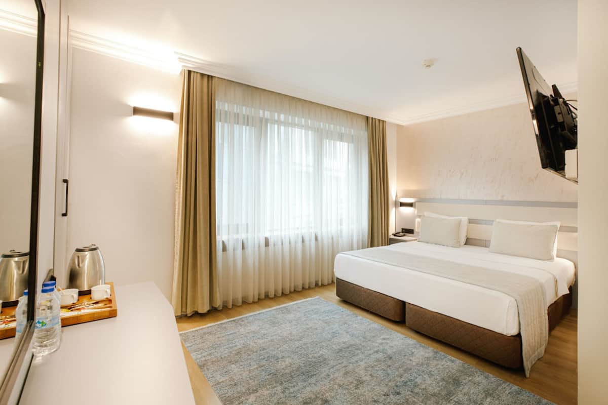 A hotel room with a bed, bedside table, curtains, and a mounted television.