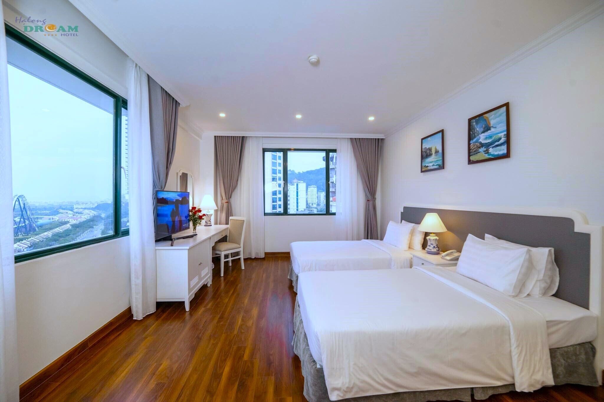 Habitació d'hotel amb dos llits, una taula de treball amb televisió, una cadira i una finestra gran amb vista a la ciutat.