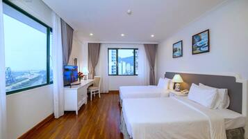 A hotel room with two beds, a desk with a TV, a chair, and a large window offering a city view.