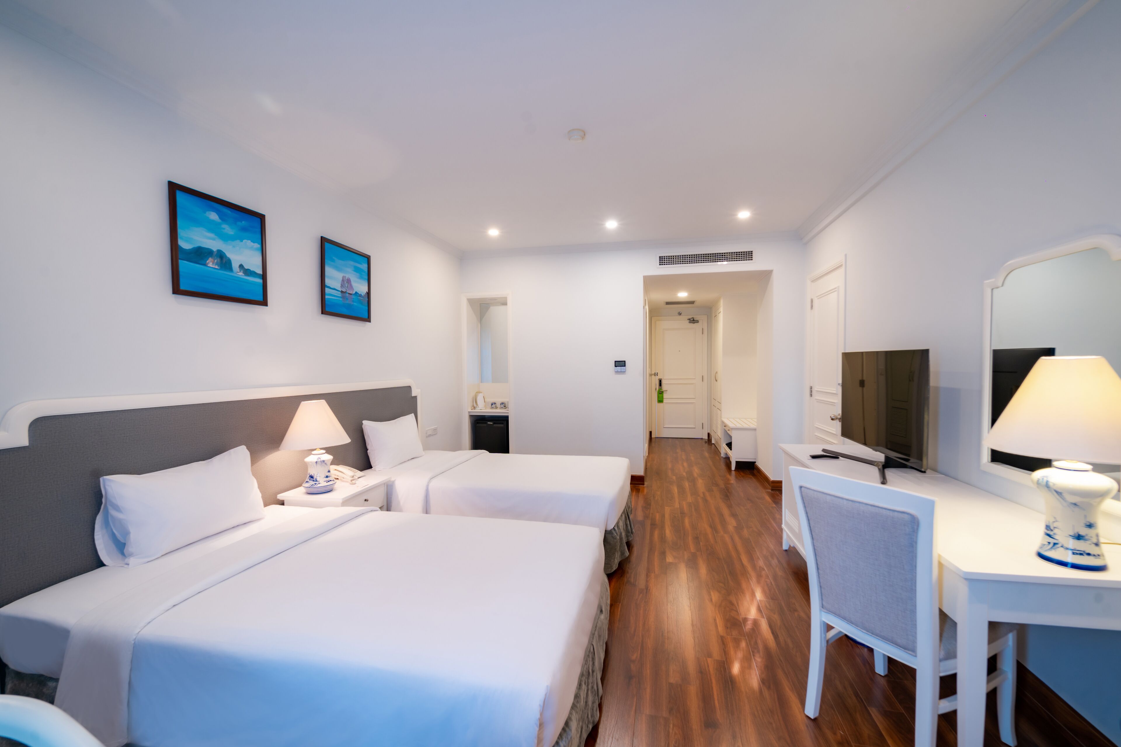 Ein Hotelzimmer mit zwei Betten, einem Schreibtisch, einem Stuhl, einem Fernseher und zwei gerahmten Bildern an der Wand.
