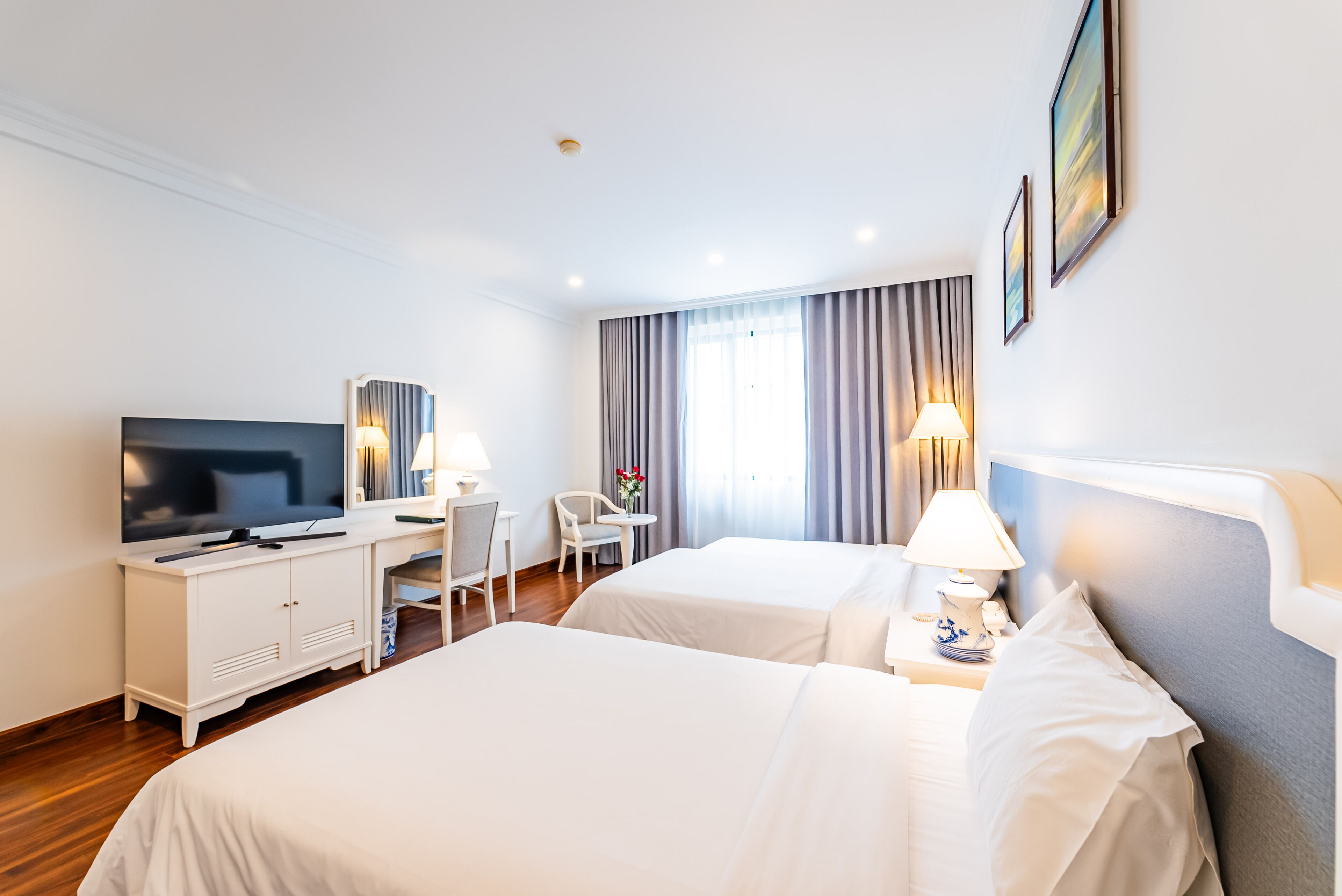 A hotel room with two beds, a desk with a television, and a chair.