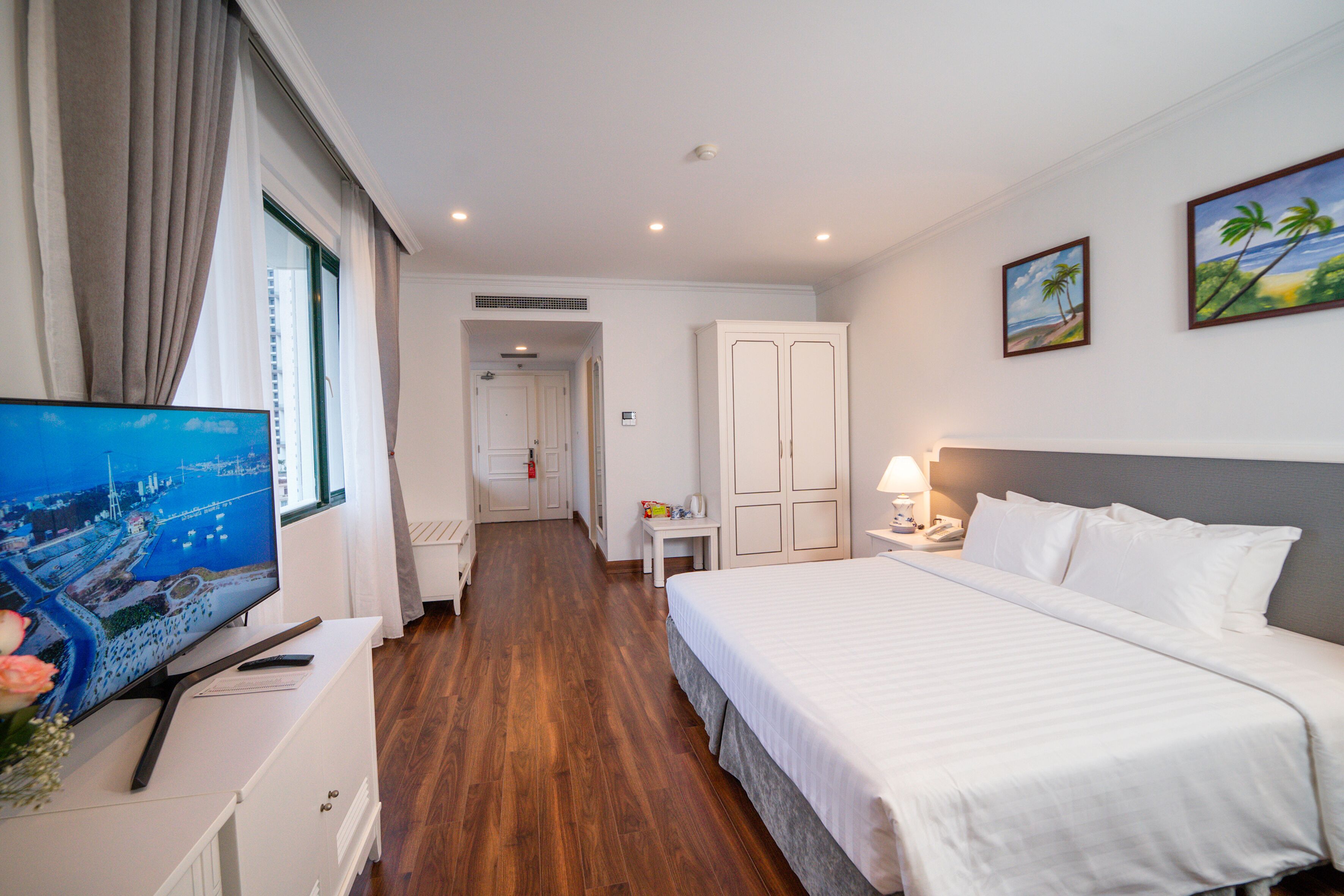 Een hotelkamer met een bed, een televisie, een bureau en uitzicht op de stad.