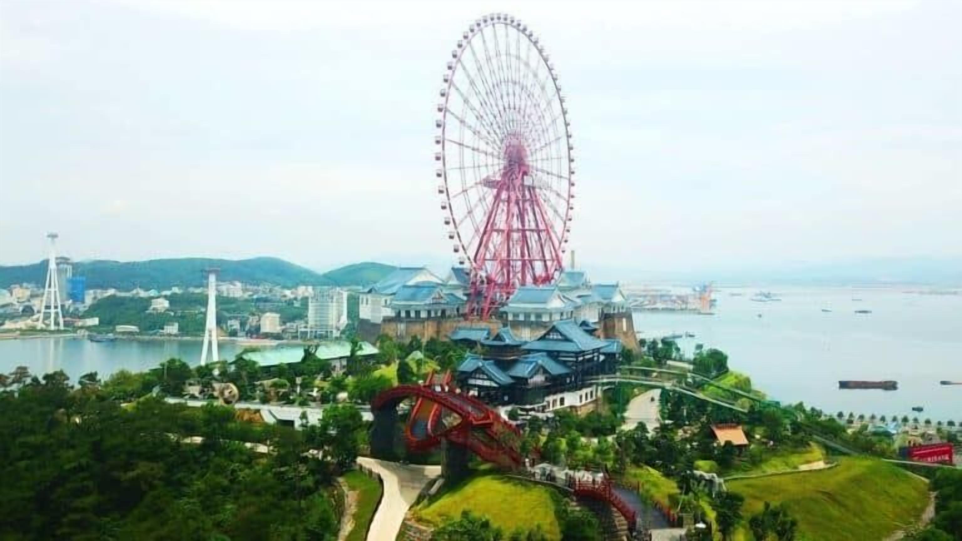 A large Ferris wheel, a roller coaster, and a body of water with buildings in the background.