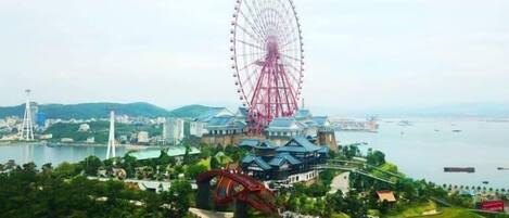 A large Ferris wheel, a roller coaster, and a body of water with buildings in the background.