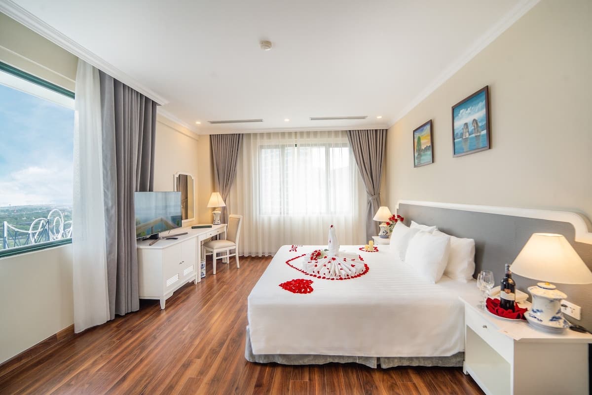 A hotel room with a large bed, a desk, a TV, and a view of a bridge.