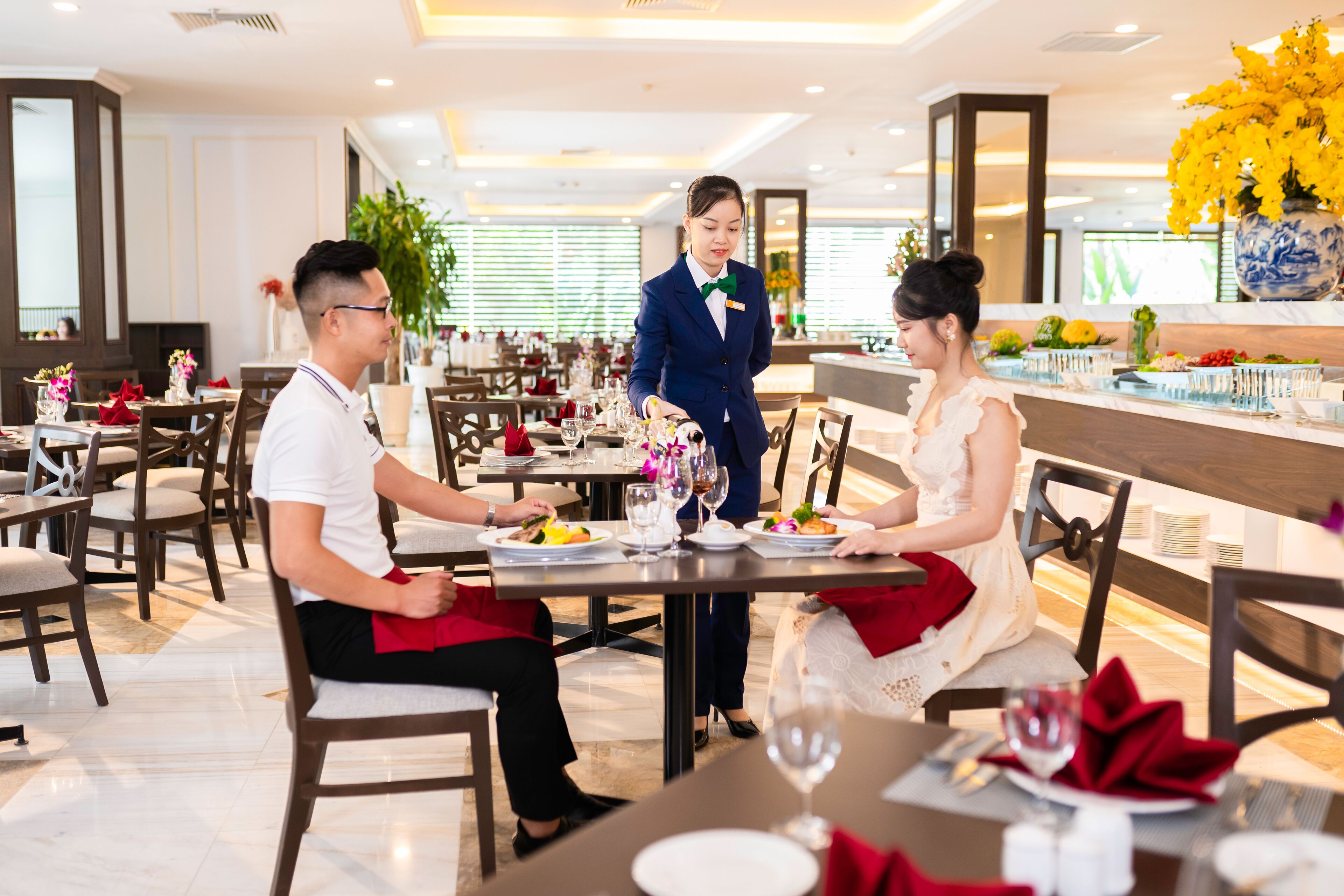 Een restaurant met meerdere tafels, elk gedekt met borden, glazen en bestek. Een ober bedient een tafel.
