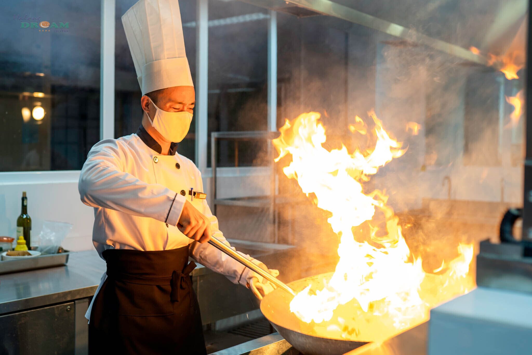 A chef performing a flambé with a pan on a kitchen counter.