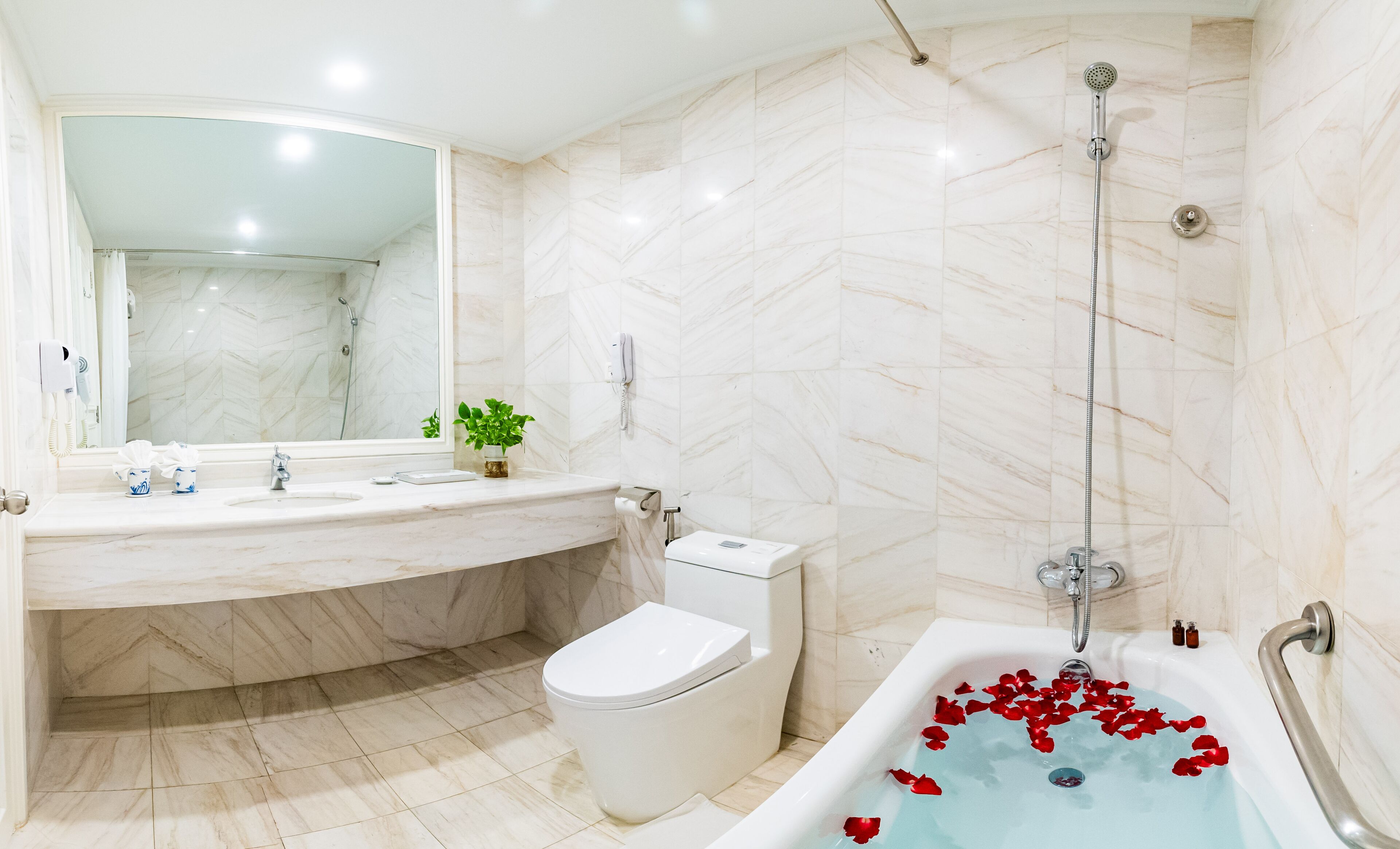 Une salle de bain moderne avec un lavabo en marbre, des toilettes et une baignoire décorée de pétales de rose.