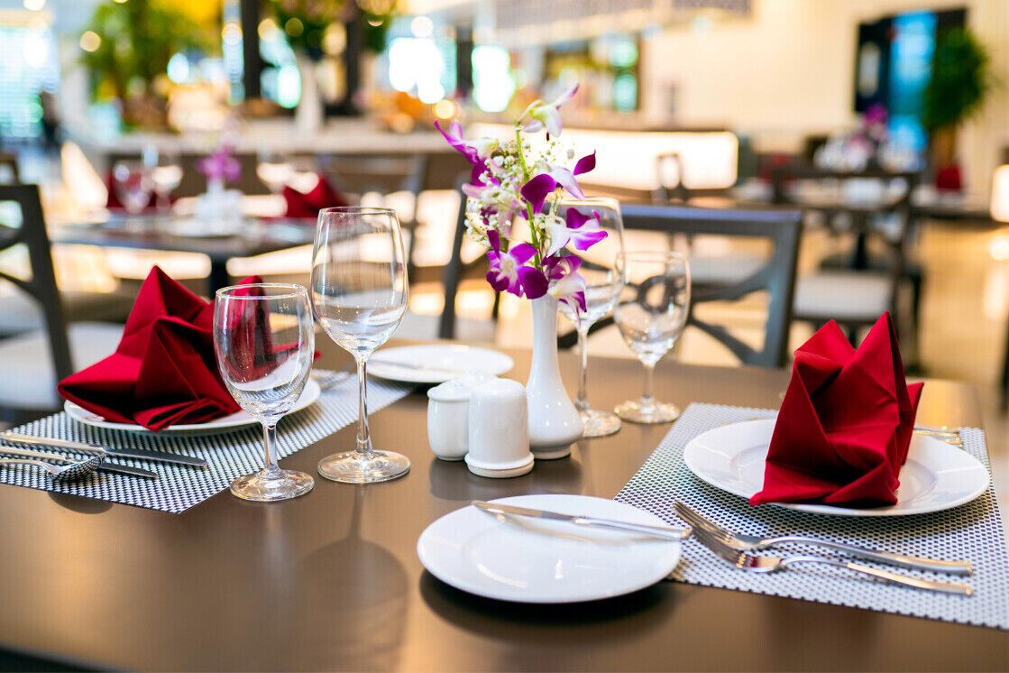A dining table set with white plates, red napkins, and clear wine glasses.