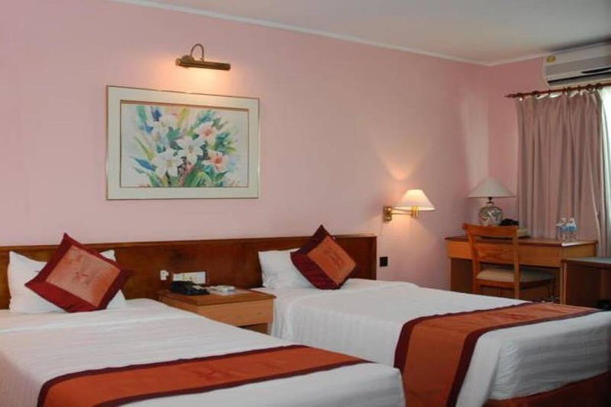 Une chambre d’hôtel avec deux lits simples, un bureau, une chaise, une lampe et un tableau au mur.