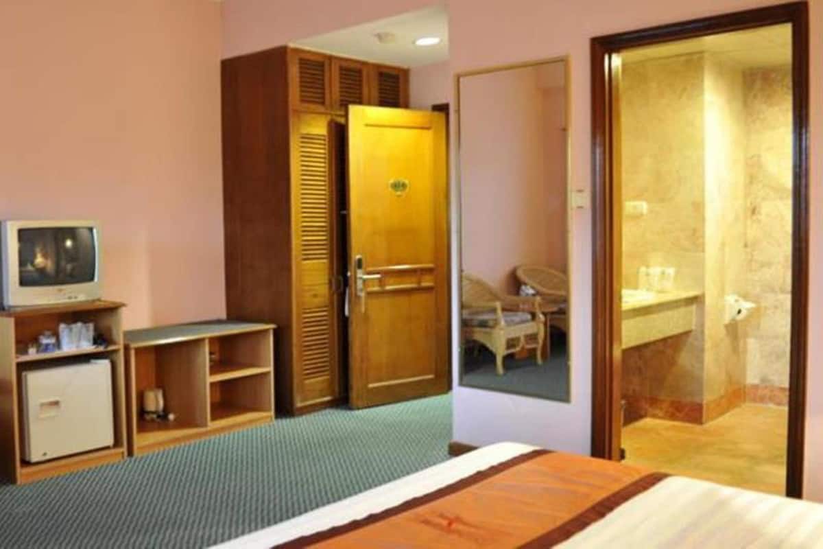 Une chambre d’hôtel avec un lit, une armoire en bois, un téléviseur et une salle de bain visible à travers une porte ouverte.