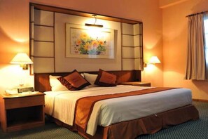 Habitación de hotel con una cama grande, dos mesitas de noche, un tocador, un cuadro en la pared y una ventana con cortinas.