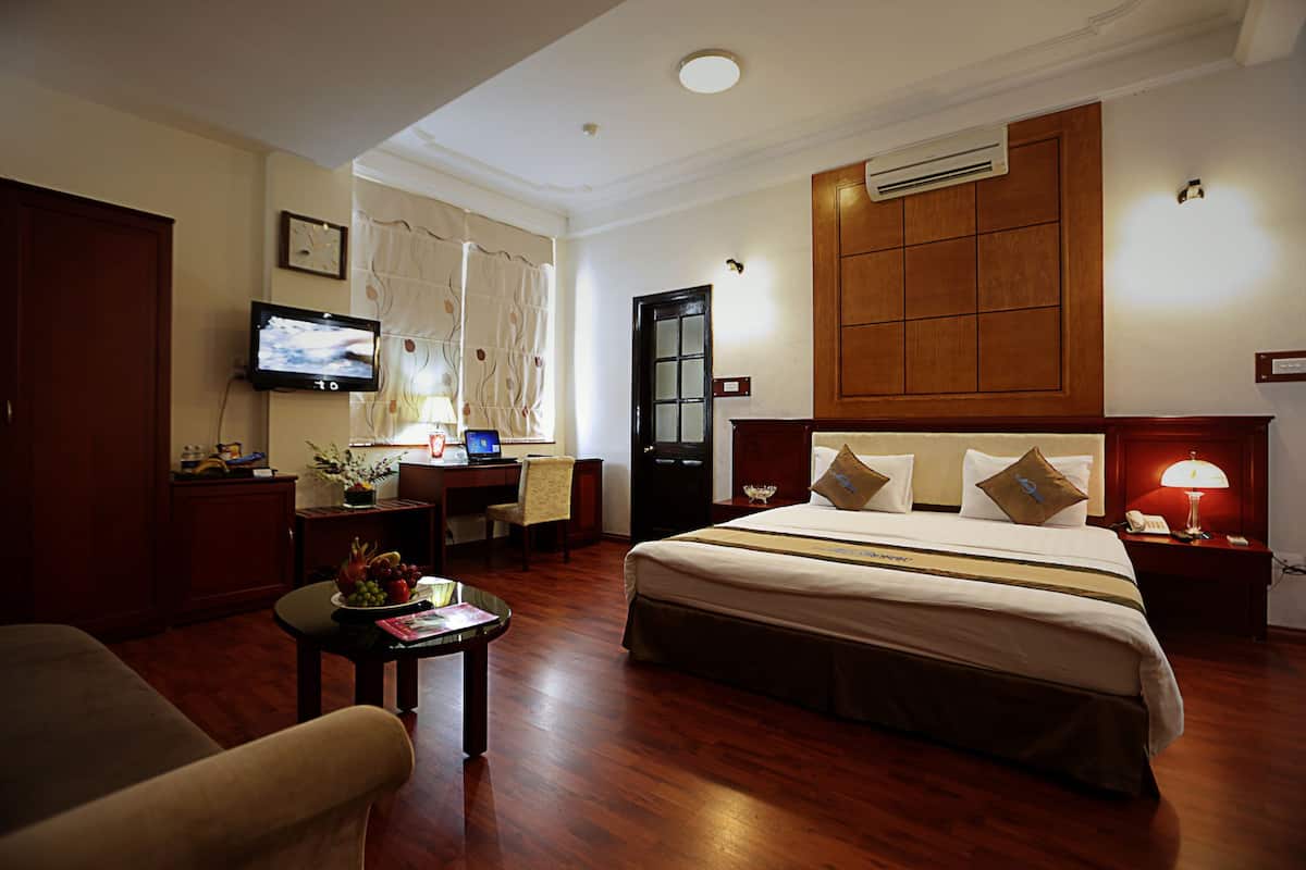 A hotel room with a large bed, a desk with a computer, a TV mounted on the wall, and a wooden wardrobe.