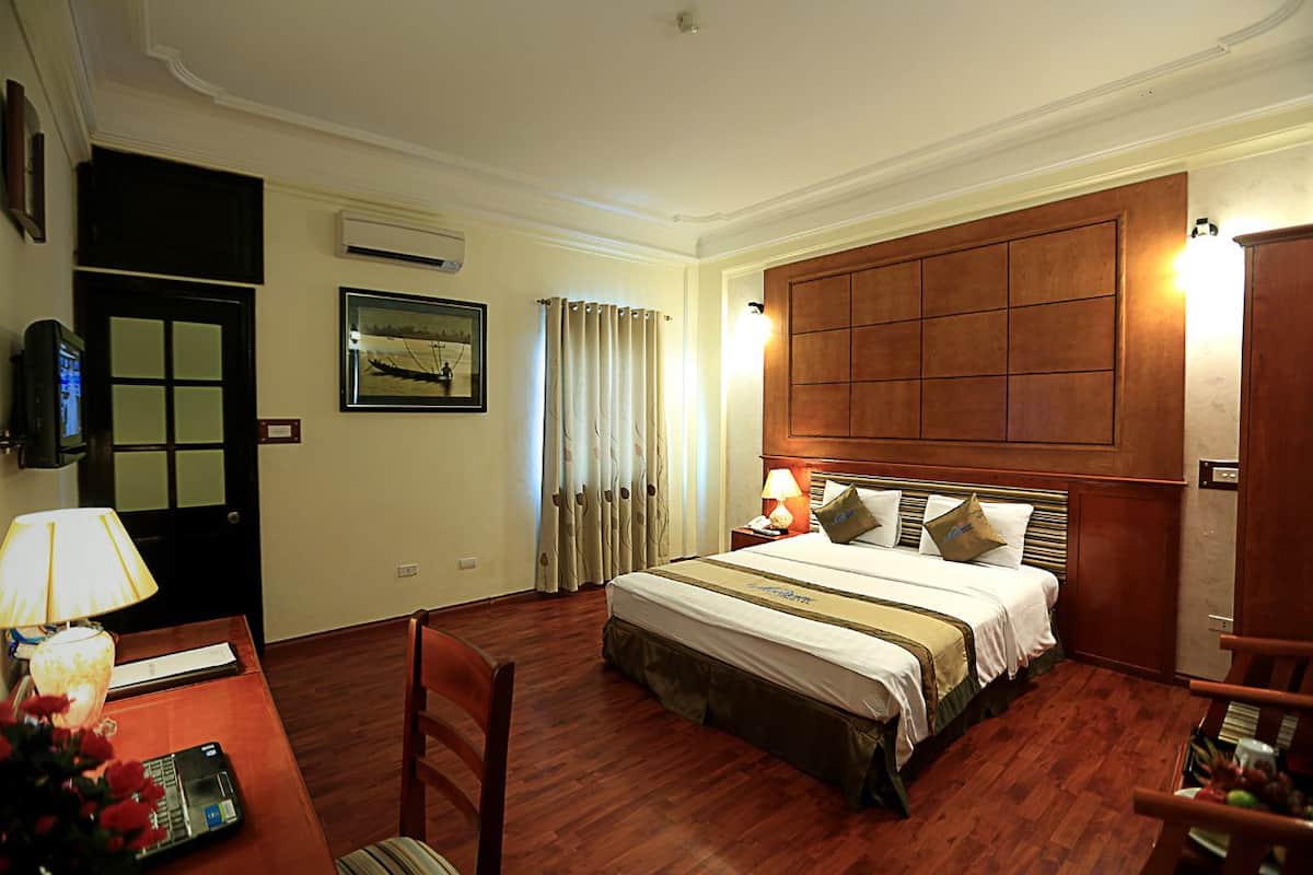 A hotel room with a large bed, a desk with a lamp, a chair, and a wooden wardrobe.