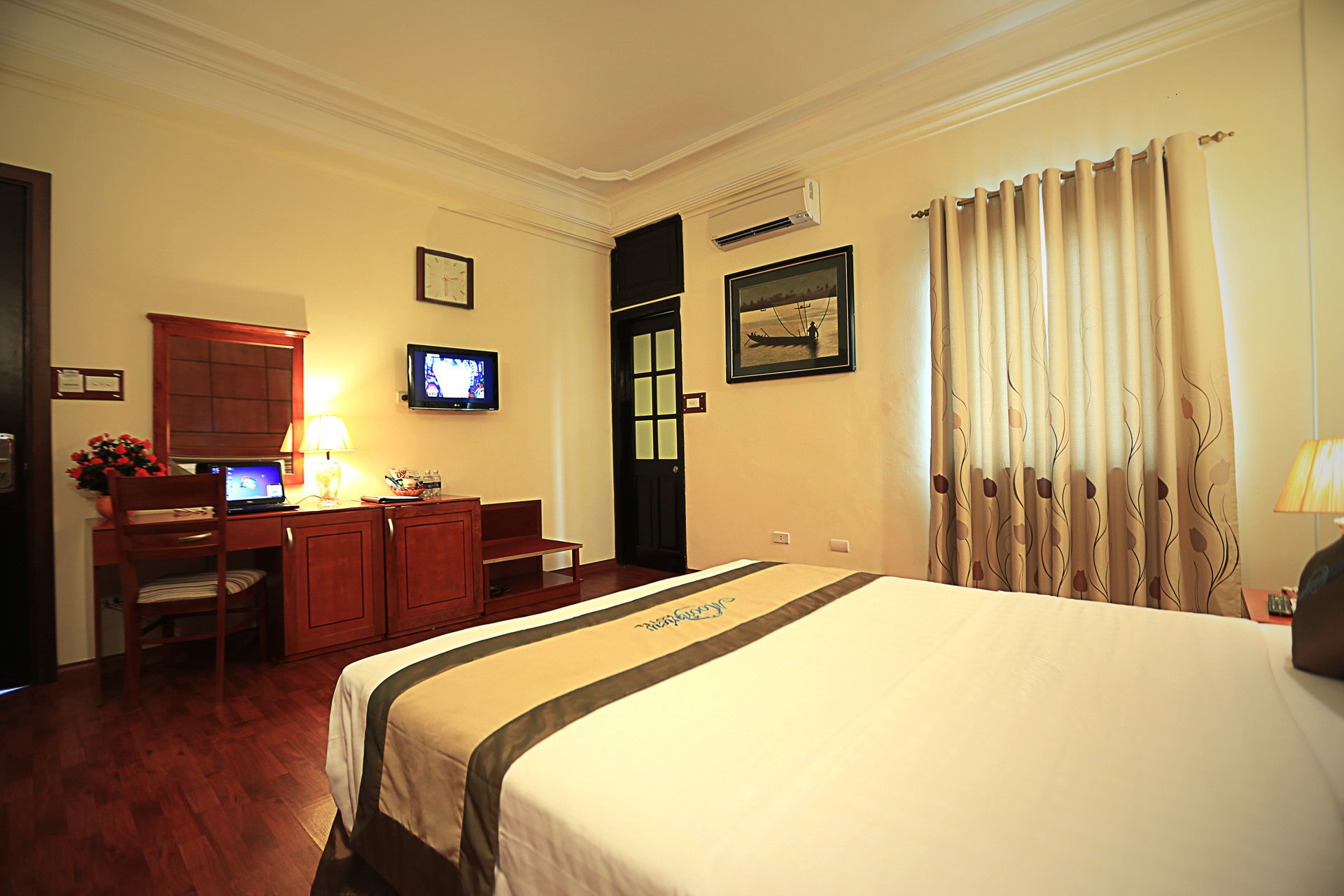 Una habitación de hotel con una cama, un escritorio con computadora, televisor y ventana con cortinas.