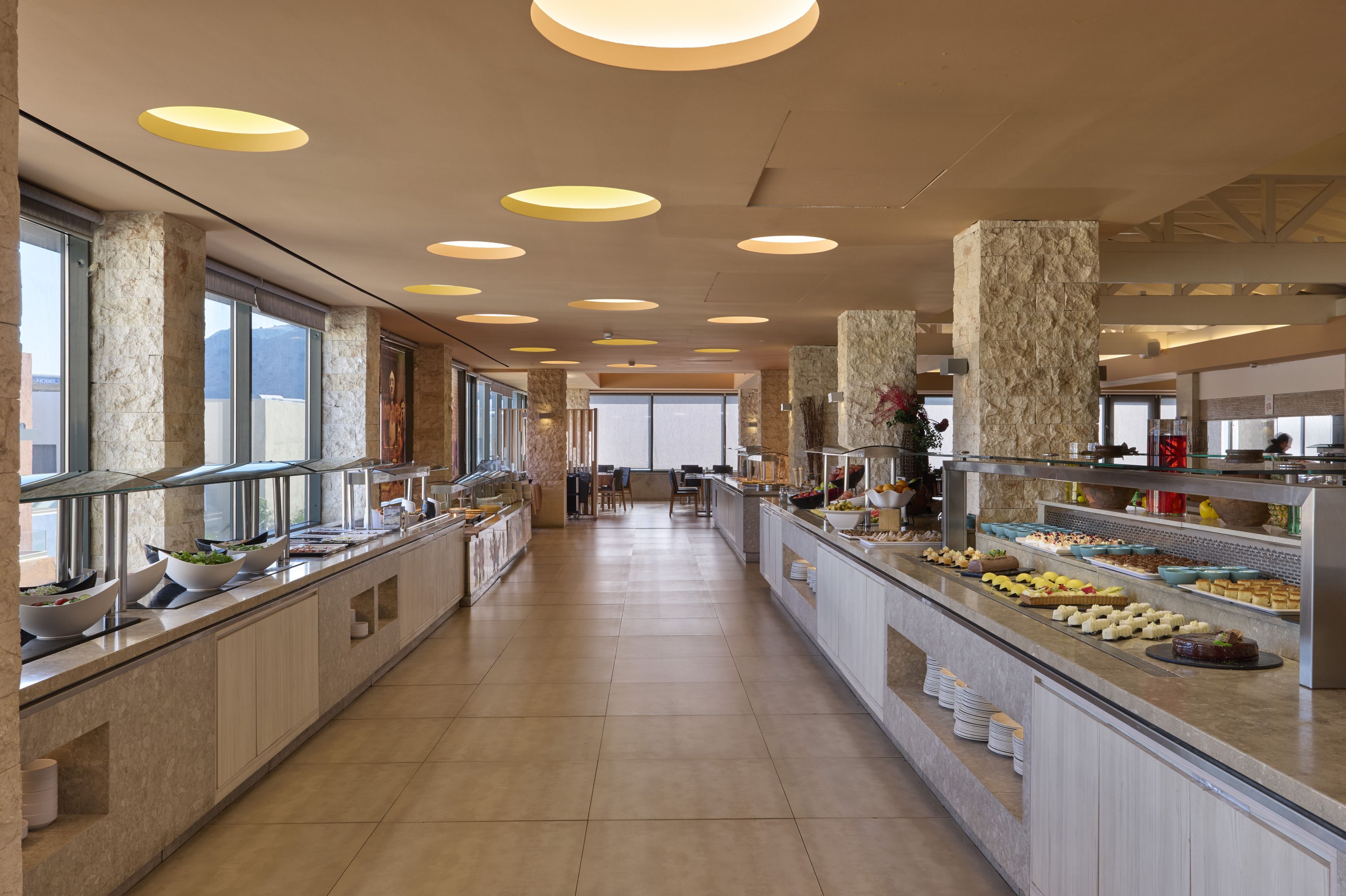 Un área amplia tipo buffet con varias estaciones de comida y diferentes disposiciones de mesas.