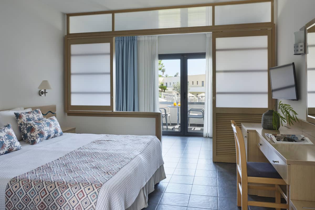 Une chambre d’hôtel équipée d’un lit, d’un bureau, d’une chaise, d’une télévision et offrant une vue sur l’extérieur.