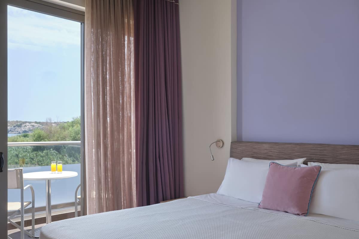 Une chambre d’hôtel avec un lit, une petite table sur laquelle sont posés deux verres de jus d’orange, et une vue sur la verdure et les collines par la fenêtre.