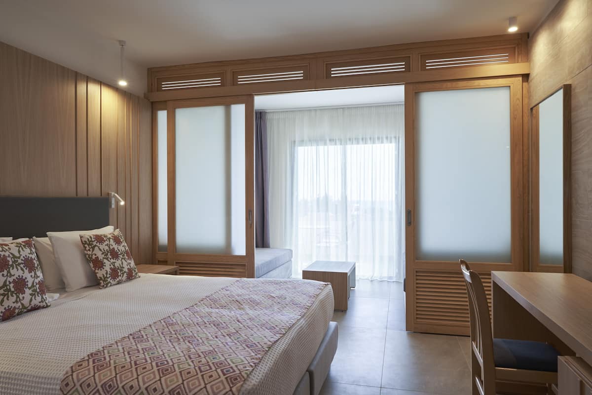 Une chambre d’hôtel moderne avec un grand lit, un bureau et une vue à travers une porte en verre dépoli.