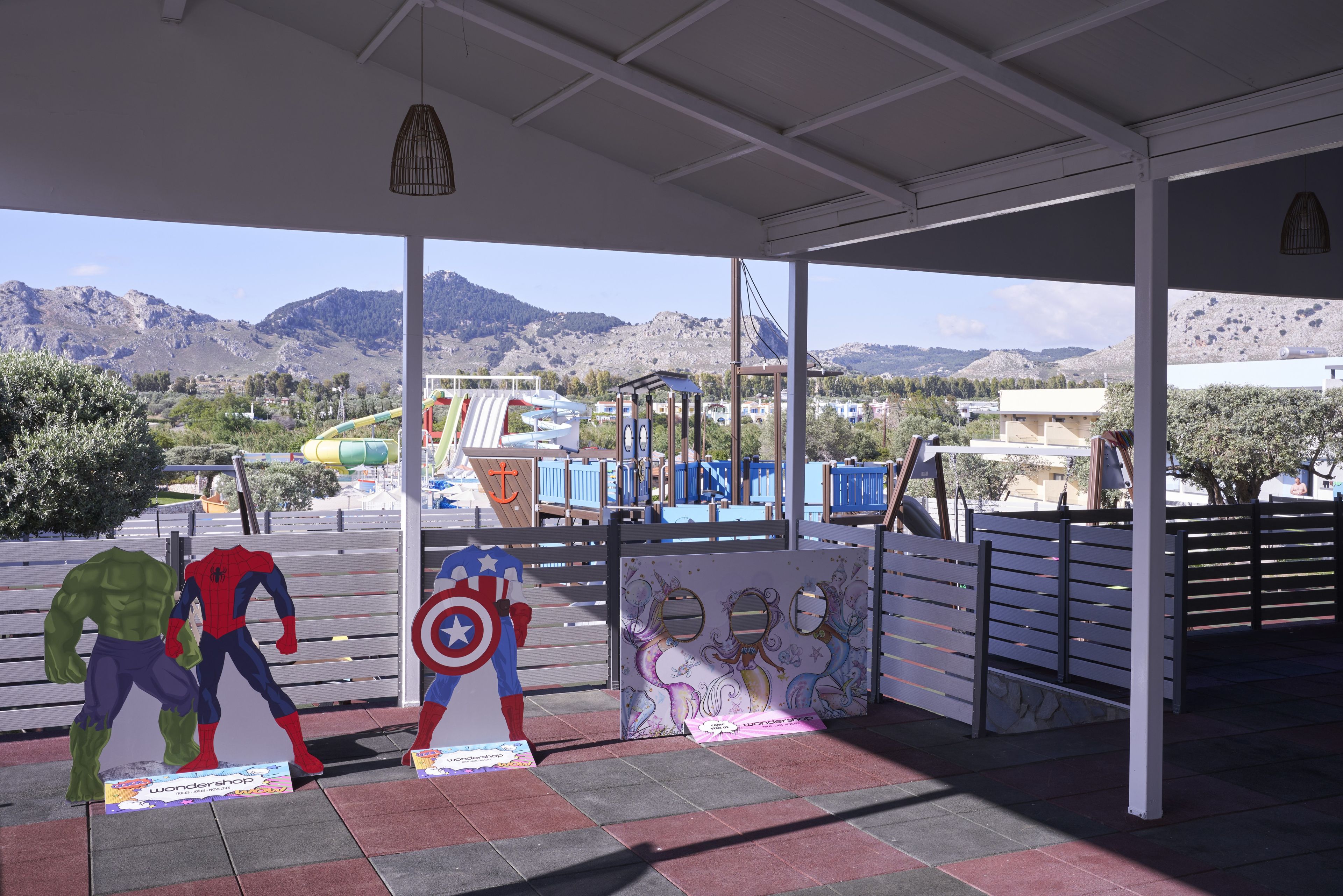 A covered outdoor area with a view of mountains, a playground with slides, and superhero cutouts.