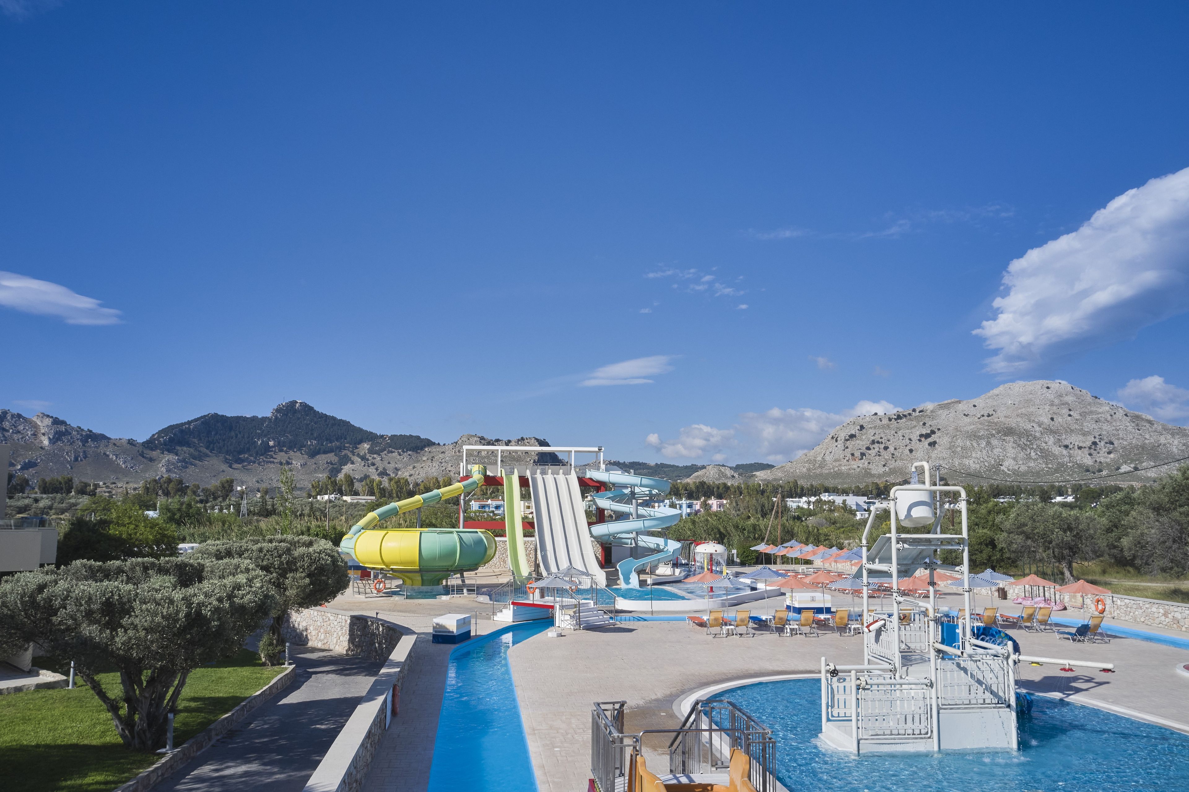 A water park with multiple slides and a swimming pool, surrounded by mountains.