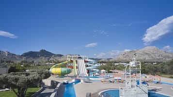 A water park with multiple slides and a swimming pool, surrounded by mountains.