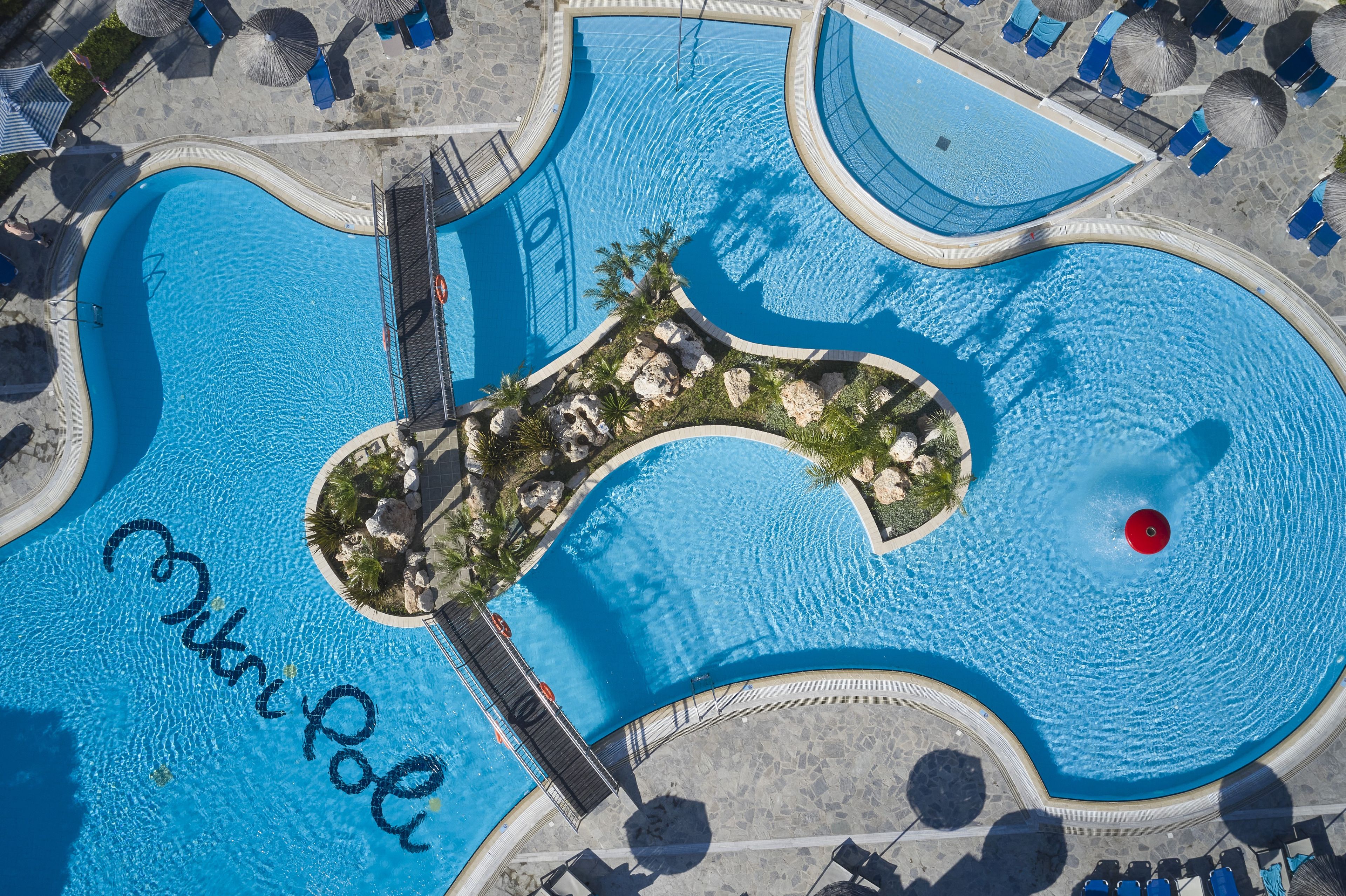 Una gran piscina curva con una isla central, rodeada de sillas de descanso y sombrillas.