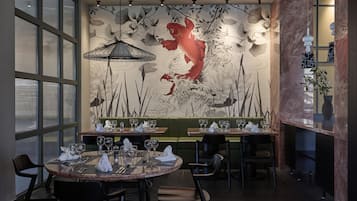 A restaurant interior with a mural of a koi fish and lotus flowers, dining tables set with glasses and cutlery, and a green booth seating area.