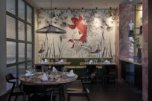En restauranginteriör med en väggmålning som föreställer karp och lotusblommor, bord uppdukade med glas och bestick samt en grön sittgrupp i form av en avskild bås.