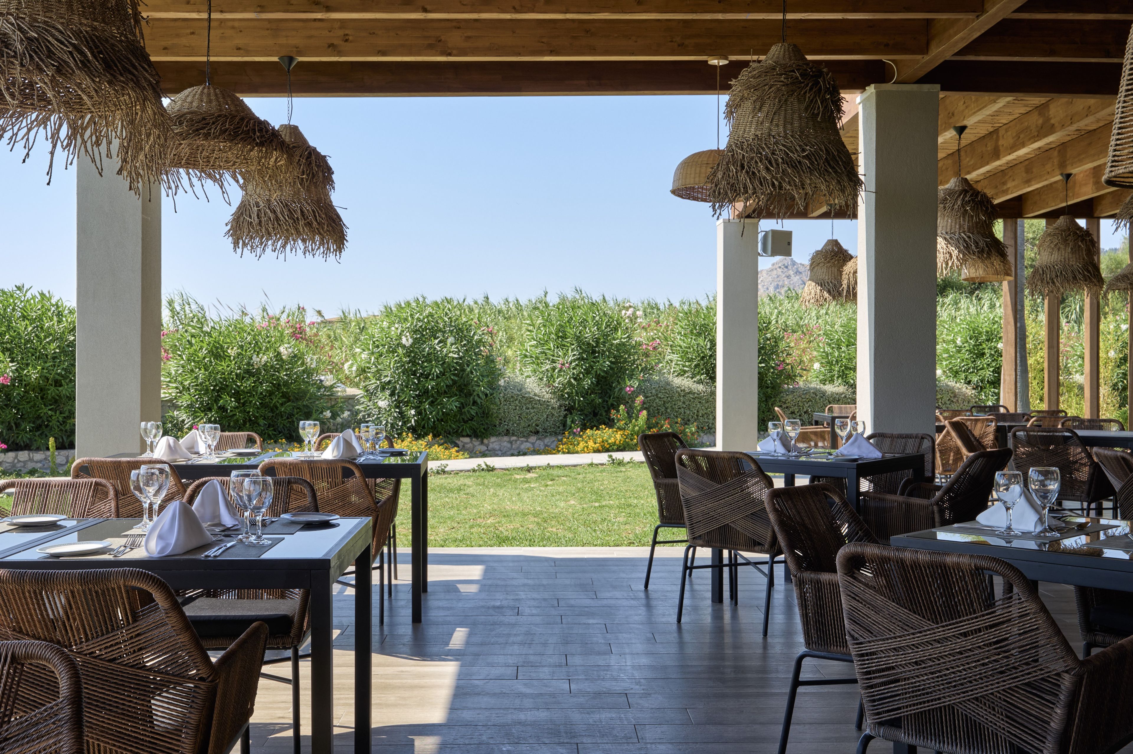 An outdoor dining area with wicker furniture and hanging lights, overlooking a landscaped garden.
