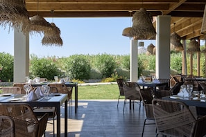 Un espace extérieur aménagé pour les repas, avec des meubles en osier et des luminaires suspendus, donnant sur un jardin paysager.