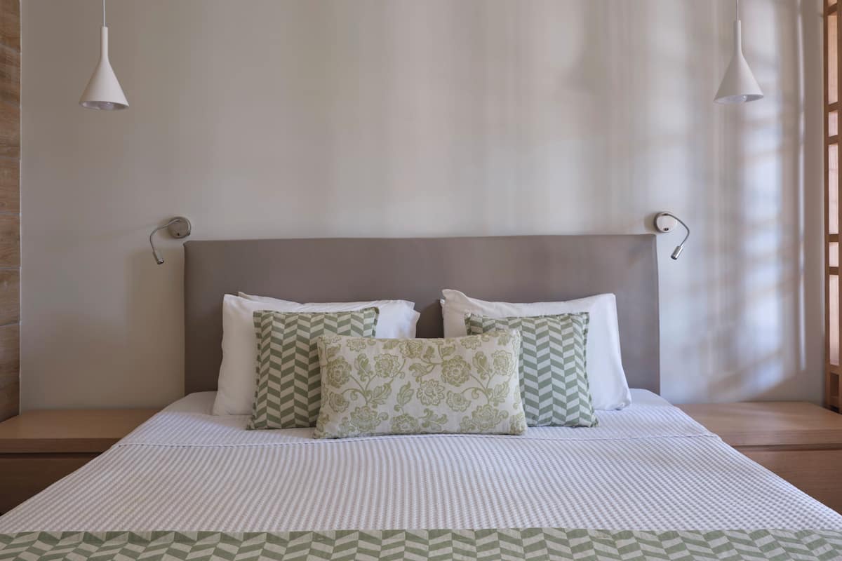 Un lit bien fait, avec une couvre-lit à rayures et des coussins décoratifs, une tête de lit sobre et deux lampes suspendues.