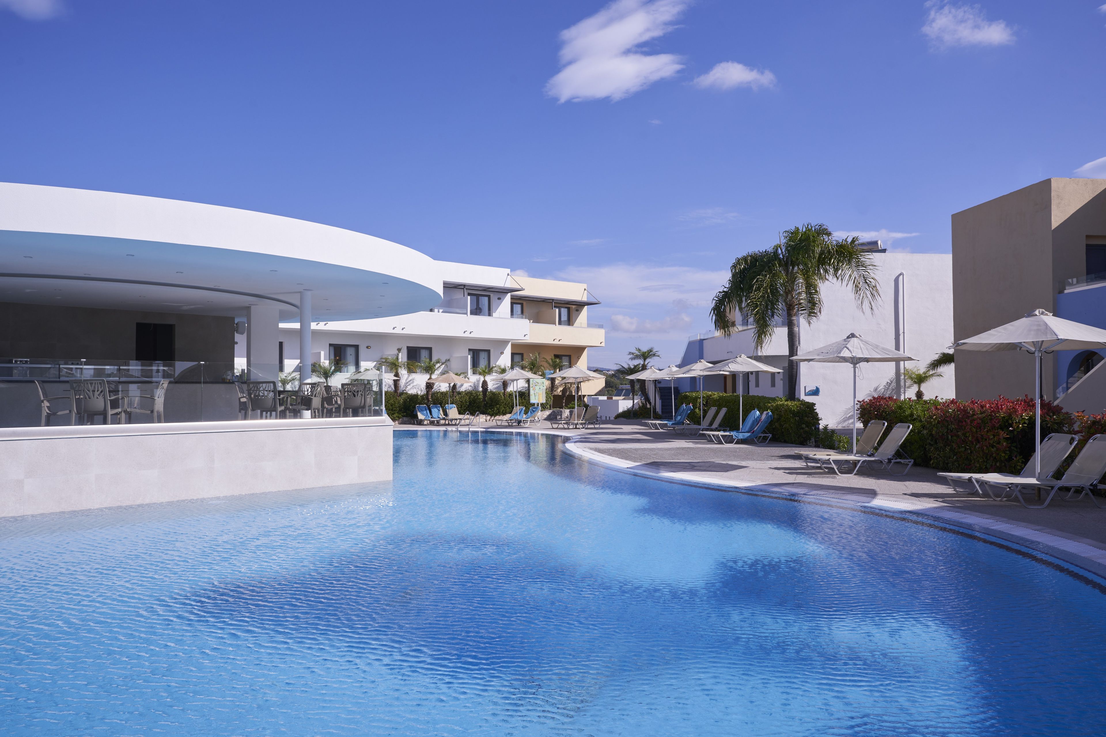 Een modern resort met een zwembad, ligbedden en een heldere blauwe lucht.