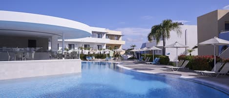A modern resort with a swimming pool, lounge chairs, and a clear blue sky.