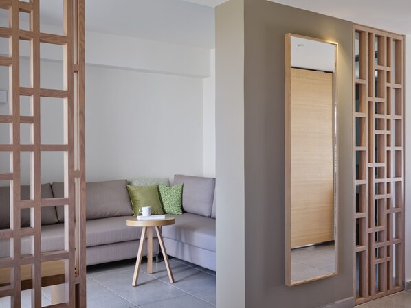 Una sala de estar moderna con un sofá gris, una mesita redonda de madera con una taza blanca y un espejo grande en la pared.
