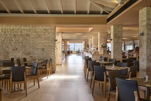 A spacious dining area with high ceilings and stone walls, featuring multiple tables and chairs arranged for dining. - Atlantica Mikri Poli Rhodes - All Inclusive (Rhodes)