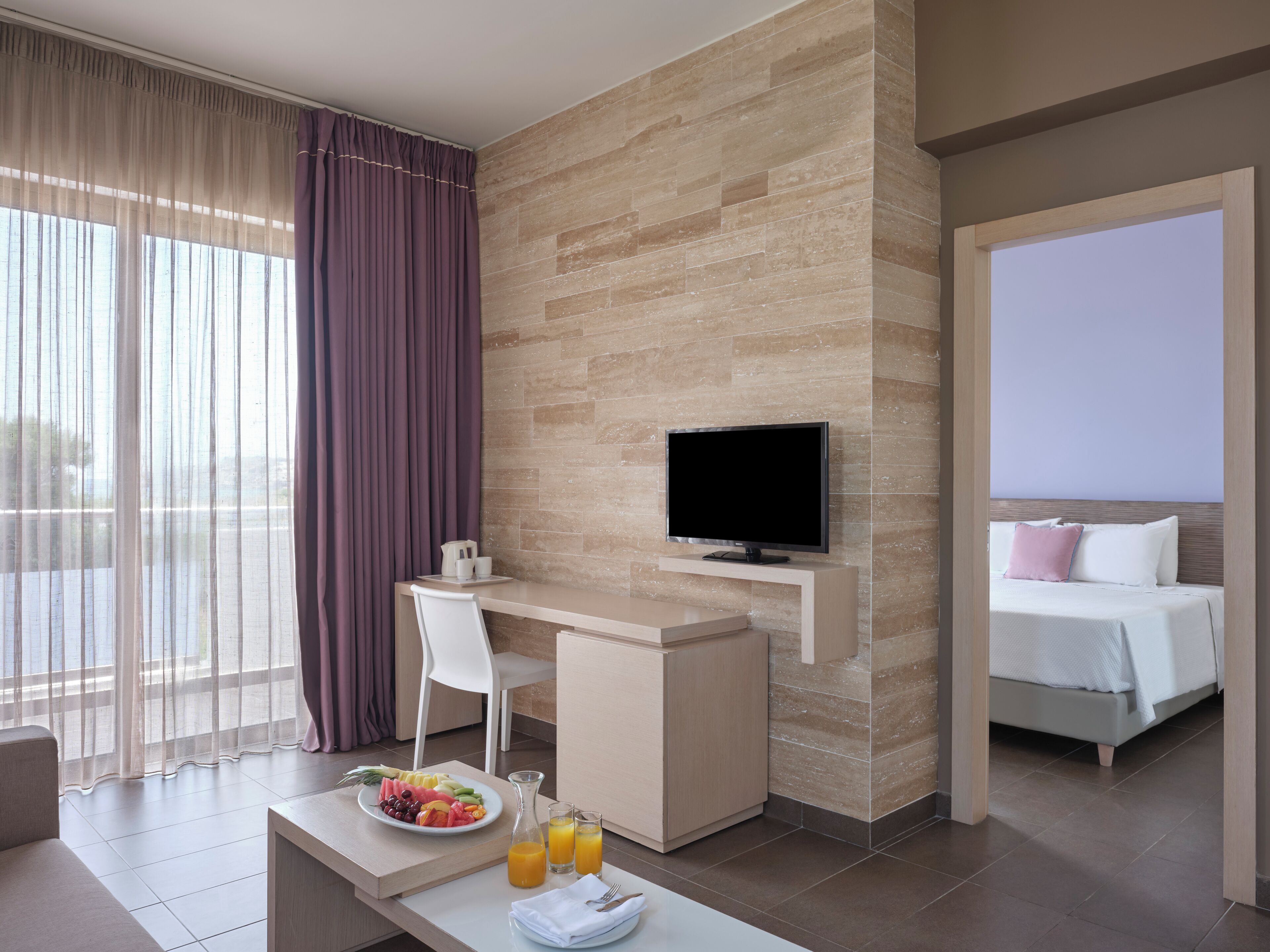 Habitación de hotel moderna con escritorio, televisor, cama y servicio de desayuno que incluye frutas y jugo.
