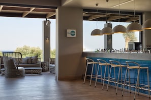 Un espace bar avec vue sur l’extérieur, des tabourets de bar et un coin salon avec des meubles en osier.