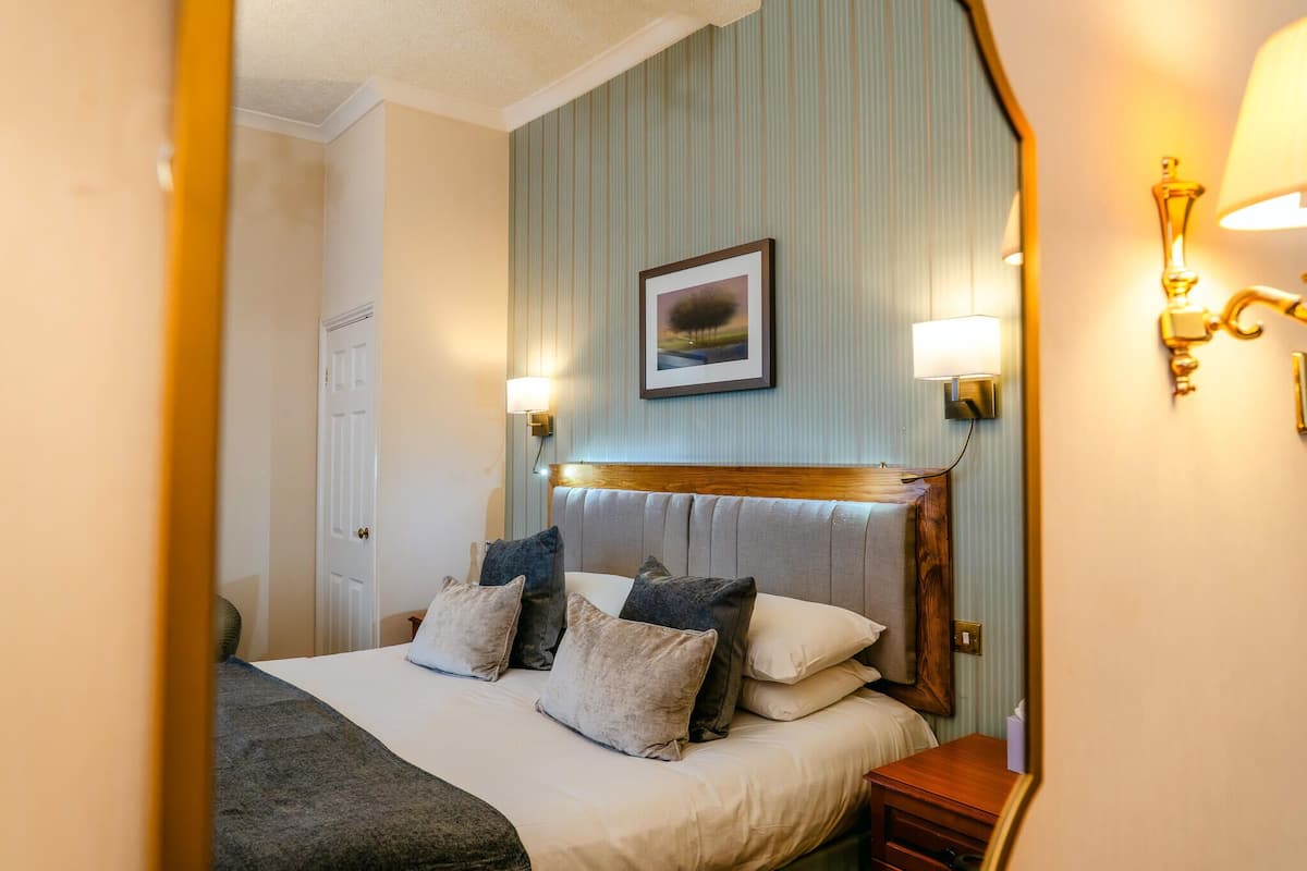 A neatly made bed with pillows, a bedside table, a lamp, and a framed picture on the wall.