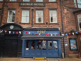 El exterior del George Hotel, con fachada de ladrillo tradicional, puerta de entrada negra y un letrero que muestra el número 1597.