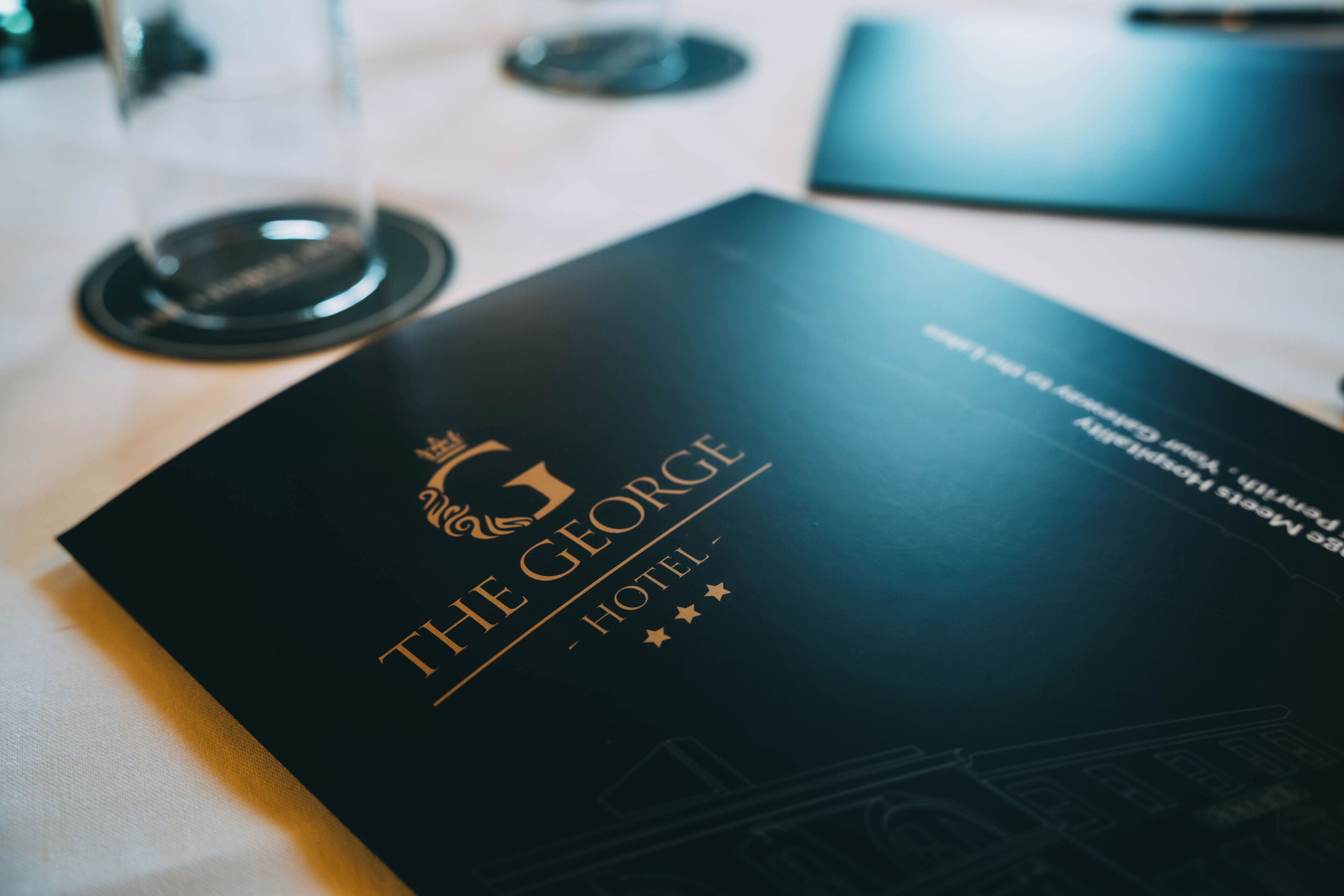 Un petit livret noir avec l’inscription « The George Hotel » et un logo représentant une couronne.