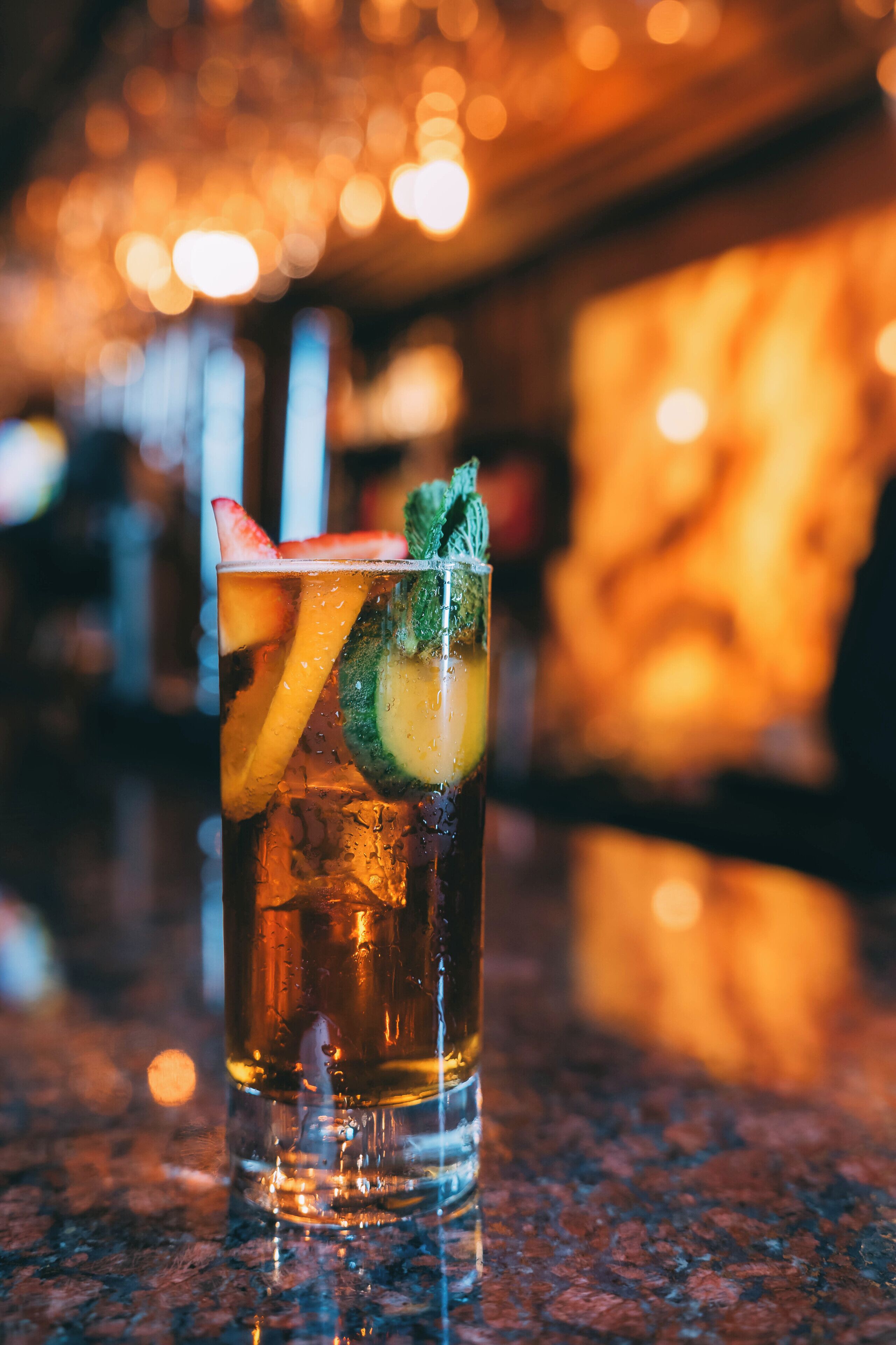 A glass with a beverage, garnished with a strawberry and mint, on a bar counter.