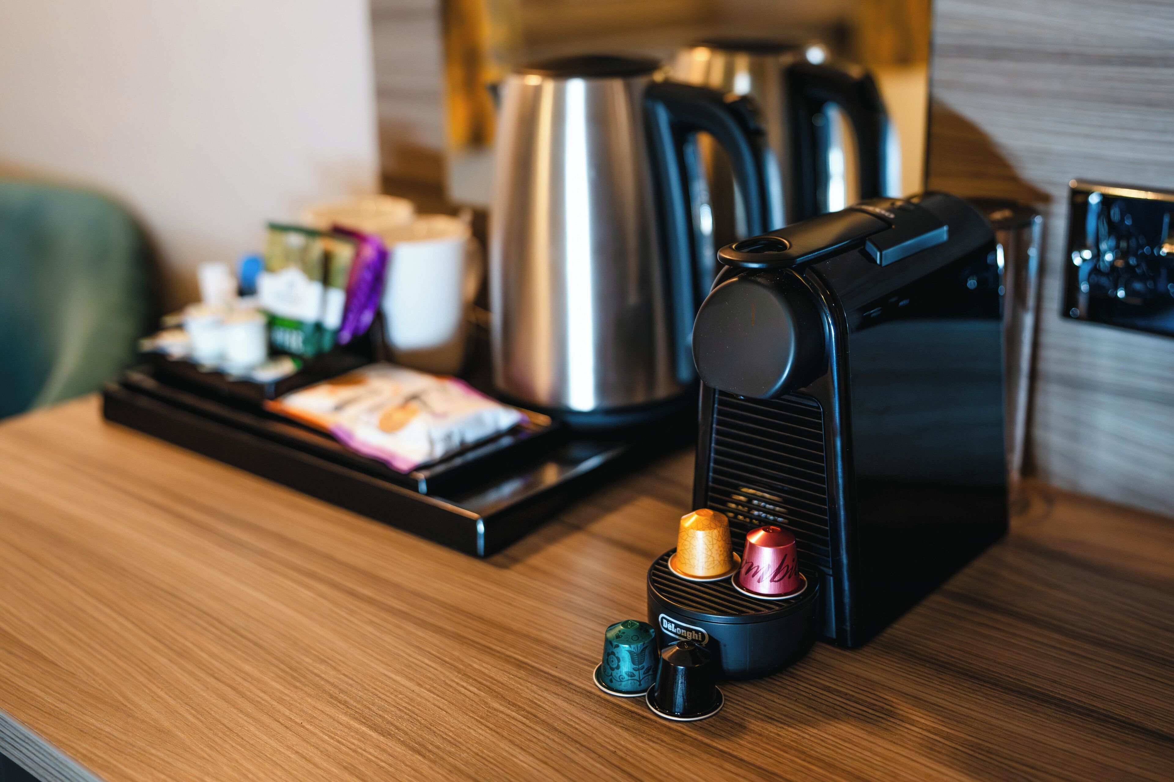 A coffee machine with a tray of coffee pods and a kettle on a wooden table.