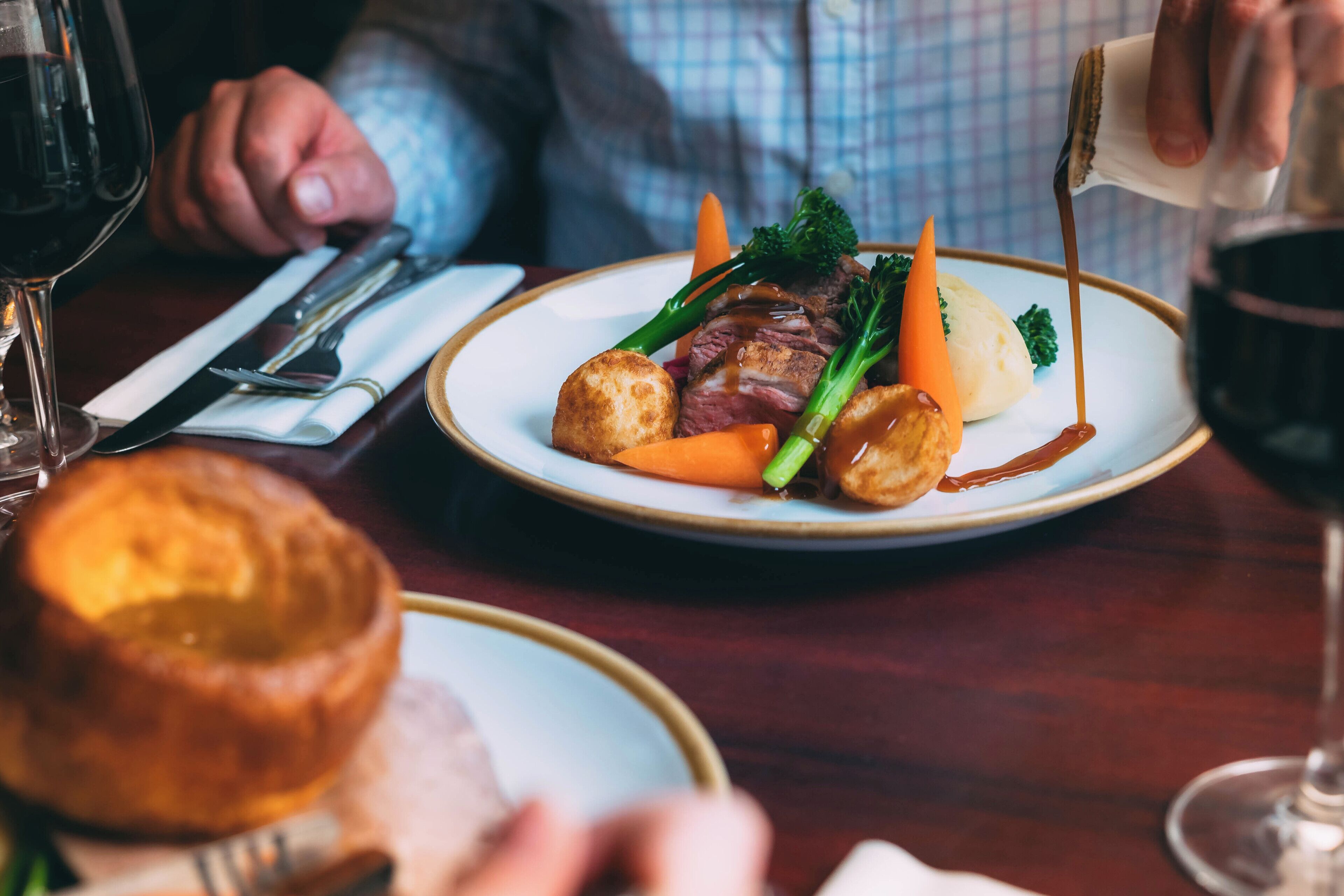 A dining table with a plate of food, a glass of red wine, and a person sitting at the table.