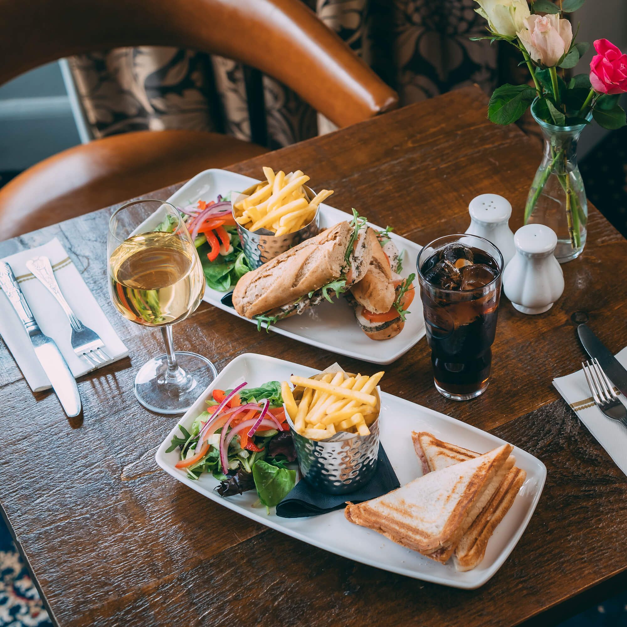 Una mesa de comedor con una comida que incluye sándwiches, papas fritas, una ensalada y una bebida.