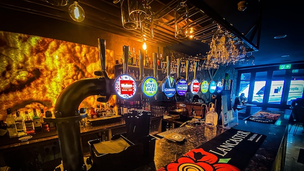 Un espace bar doté de plusieurs robinets à bière, d’un comptoir où sont exposées diverses bouteilles, et d’un motif floral remarquable sur le sol.