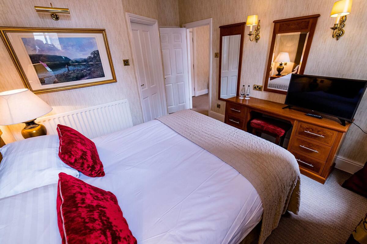 A hotel room with a large bed, a dresser, a television, and a mirror.