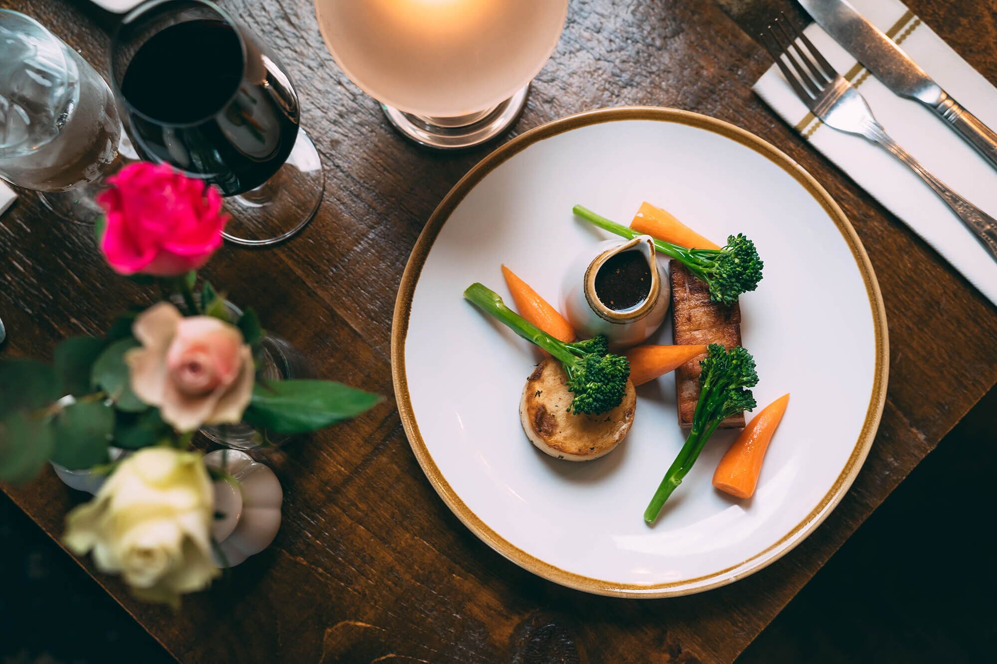 A plate of food with vegetables and a small bowl of sauce on a wooden table.