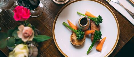 A plate of food with vegetables and a small bowl of sauce on a wooden table.